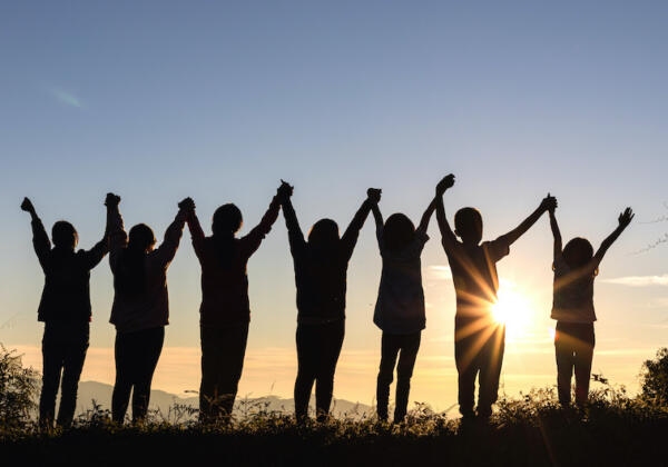 Silhouette Of Happy Children Standing With Raised Hands On The Mountain At The Sunset Time.